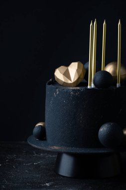 Altın çikolata küreleri, kalp ve mumlarla süslenmiş siyah kadife kaplı lüks yıldönümü pastası. Siyah arka planda sevilen için klasik pasta.