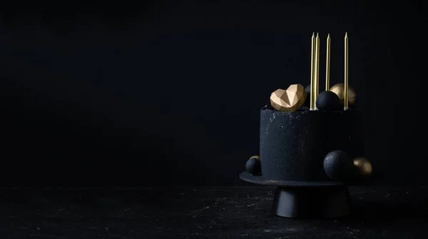 stock image Luxury anniversary cake with black velvet sprayed coating decorated with golden chocolate spheres, heart and candles on top. Vintage cake for beloved one on the black background