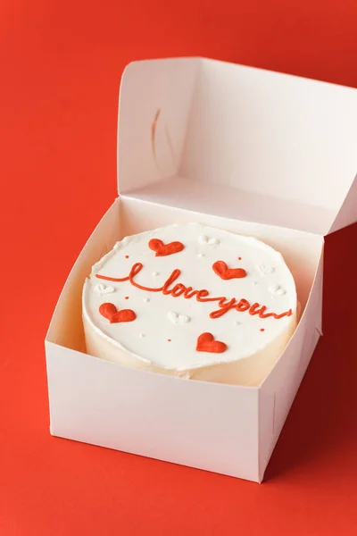 Korean style bento cake in a white gift box on the red festive background. Little cake with I love you inscription. Happy Valentine\'s Day