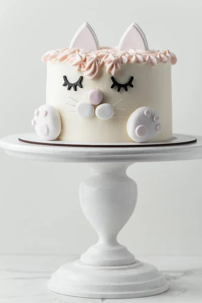 白い背景に食用のまぶた 耳と魔法の足で飾られた小さな女の子のための猫のケーキ 白とピンクのクリームチーズの霜降り誕生日ケーキ — ストック写真