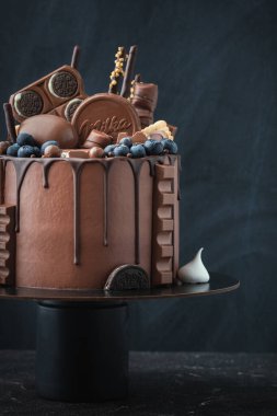 KYIV, UKRAINE - January 31: Birthday cake with brown cream cheese frosting and chocolate drips decorated with Kinder egg toy, Milka and KitKat sweets, Oreo cookies and Toblerone candy on black