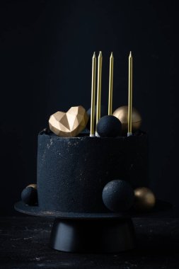 Altın çikolata küreleri, kalp ve mumlarla süslenmiş siyah kadife kaplı lüks yıldönümü pastası. Siyah arka planda sevilen için klasik pasta.