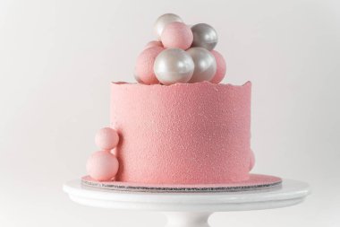Beyaz arka planda gümüş ve pembe çikolata küreleriyle süslenmiş pembe kadife kaplı doğum günü pastası.