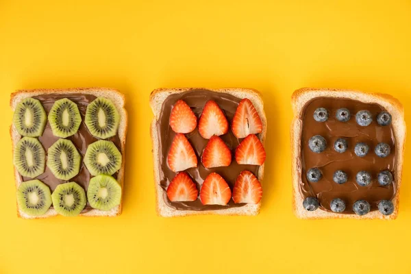 顶部的白色土司面包片与巧克力榛子铺上新鲜的夏季浆果 蓝莓和猕猴桃黄色背景 早上早餐的概念 — 图库照片