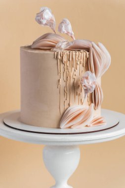 Yenebilir şeker çiçekleriyle süslenmiş bej çikolata kremalı ve bej arka planda yenilebilir kağıt dekoru olan güzel büyük bir pasta..