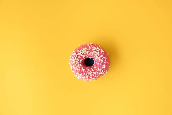 Top view of donut with pink chocolate icing on the yellow background. Morning breakfast concept. Food mockup with copy space for a free text. Flat lay. Donut covered with pink glaze