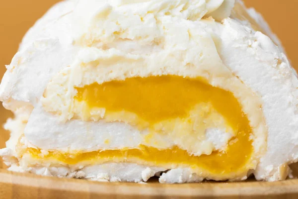 Close-up of homemade meringue roll filled with mango puree on the beige background. Meringue roulade with yellow fruit filling in the bamboo wooden plate. Macro shot. Textured background