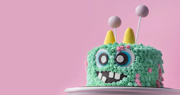 Monster theme cake on the pink background. Funny birthday cake with turquoise fluffy cream cheese frosting. Spooky monster pastry with edible fur. Happy Halloween party