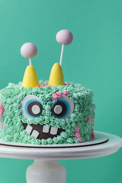 Monster theme cake on the turquoise background. Funny birthday cake with turquoise fluffy cream cheese frosting. Spooky monster pastry with edible fur. Happy Halloween party