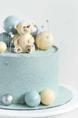 Cake with blue or turquoise velvet cream coating with teddy bear on top. Birthday cake for a little baby with chocolate turquoise and silver spheres on the white background. One year old celebration.