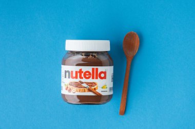 KYIV, UKRAINE - 21 Şubat: Nutella çikolatalı fındık, cam bir kavanoza serpilmiş, yanında beyaz kaşık ve mavi fındık var. Üst Manzara. Boşluğu kopyala.