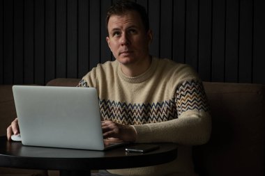 Genç beyaz adam modern bir çalışma alanında dizüstü bilgisayar kullanarak konsantre oldu. Mektup yazarken ve klavyede yazarken başarılı bir serbest yazar