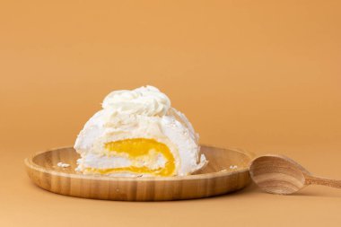 Ev yapımı kremalı pasta dilimi mango püresiyle doldurulmuş ve bej arka planda badem gevreğiyle süslenmiş. Bambu ahşap tabakta sarı meyveli krema rublesi.