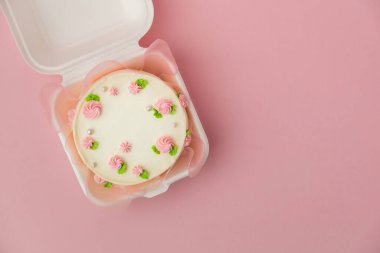 Krem şantili pembe çiçeklerle süslenmiş beyaz krem peynirli küçük geleneksel Kore usulü bento keki. Pembe pastel arka planda beyaz hediye kutusunda küçük bir bahar pastası. Üst görünüm