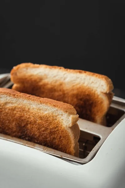 在黑色背景上 从烤面包机上伸出的少许烧焦的白面包烤面包的特写镜头 准备好了 用深色的外壳烤面包 早上早餐的概念 — 图库照片