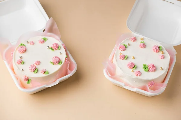Small traditional Korean style bento cake with white cream cheese frosting decorated with pink whipped cream flowers. Little spring cake in the white gift box on the beige background
