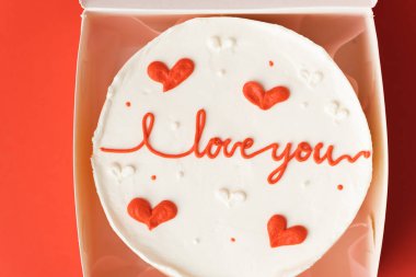 Korean style bento cake in a white gift box on the red festive background. Little cake with I love you inscription. Happy Valentine's Day. Flat lay