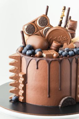 KYIV, UKRAINE - January 31: Birthday cake with brown cream cheese frosting and chocolate drips decorated with Kinder egg toy, Milka and KitKat sweets, Oreo cookies and Toblerone candy on white