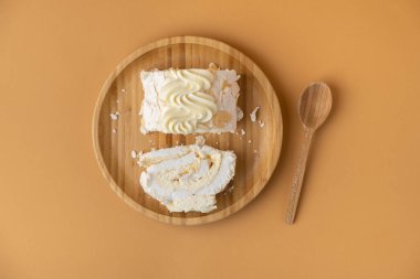 Ev yapımı kremalı pasta dilimi mango püresiyle doldurulmuş ve kahverengi arka planda badem gevreğiyle süslenmiş. Bambu ahşap tabakta sarı meyveli krema. Üst görünüm