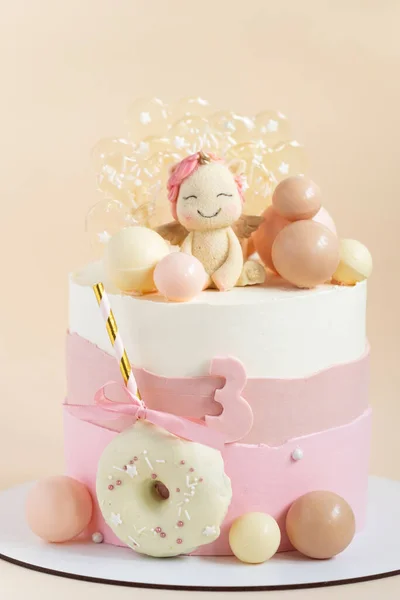 女の子のための誕生日ケーキピンクのパステルクリームチーズの霜で飾られたユニコーンフィギュア チョコレート球とキャラメルキャンディーベージュの背景に — ストック写真