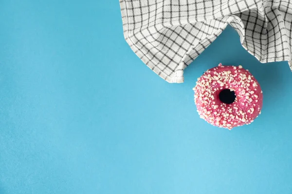 Top view of donut with pink chocolate icing on the blue pastel background. Morning breakfast concept. Food mockup with copy space for a free text. Flat lay. Donut covered with pink glaze