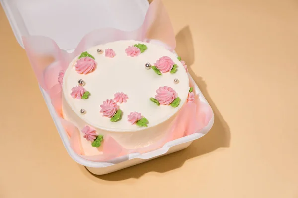 ベージュを背景に白いギフトボックスにピンクのクリームチーズの花で飾られた小さな韓国スタイルのトレンディーなお弁当ケーキ 最愛の人への贈り物としてケーキ 女性のための春の柔らかいケーキ トップ表示 — ストック写真