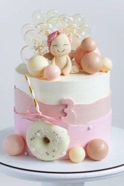 Beyaz arka planda tek boynuzlu at figürü, çikolata küreleri ve karamel şekerlerle süslenmiş pembe pastel krem peynirli bir kız için doğum günü pastası..