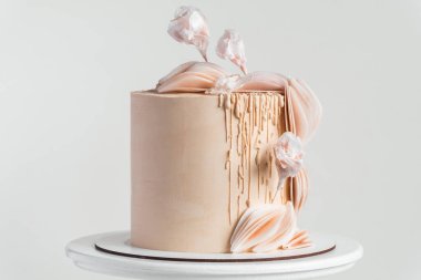 Yenebilir şeker çiçekleriyle süslenmiş bej çikolata kremalı ve beyaz arka planda yenilebilir kağıt desenli güzel bir pasta..