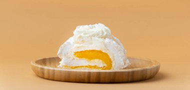 Ev yapımı kremalı pasta dilimi mango püresiyle doldurulmuş ve bej arka planda badem gevreğiyle süslenmiş. Bambu ahşap tabakta sarı meyveli krema rublesi.