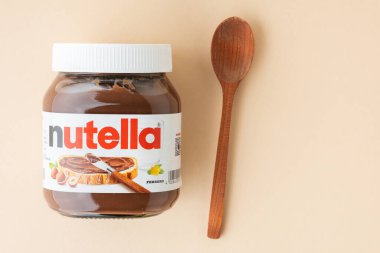 KYIV, UKRAINE - 21 Şubat: Nutella çikolatalı fındık, beyaz kaşık ve bej arkaplana saçılmış çiğ fındıklar ile cam bir kavanoza serpiştirildi. Üst Manzara. Boşluğu kopyala.