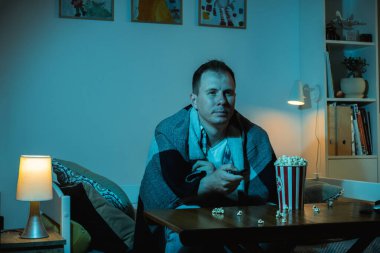 Adam TV izliyor ve gece evde patlamış mısır yiyor. Bir kanepede oturan bir adamın portresi. Kocaman bir televizyonun mavi ekran ışığıyla dolu bir odada.