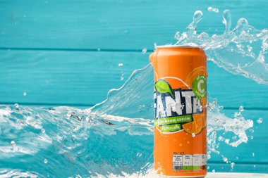 KYIV, UKRAINE - 13 Mayıs: Turkuaz ahşap arka planda klasik Fanta portakal kutusunun üzerine su sıçraması yakın çekim. Meşrubat reklamı. Yazın soğuk, ferahlatıcı bir içecek..