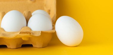 Sarı arkaplandaki kahverengi kutunun içindeki beyaz yumurtaları yakın plan çek. Makro atış. Boş metin için boşluk kopyala.