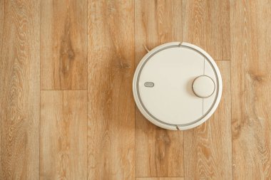 Robot elektrikli süpürge oturma odasındaki ahşap döşemede çalışıyor. Otomatik beyaz elektrikli süpürge robotu. Ücretsiz metin için boşluk kopyala. Düz yatıyordu
