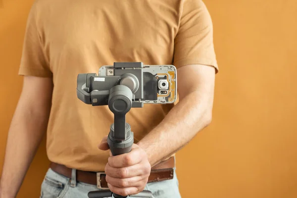 stock image Man filming with a smartphone using a gimbal stabilizer on yellow background. Using three-axis electronic stabilizer to make vlogs or video shooting.