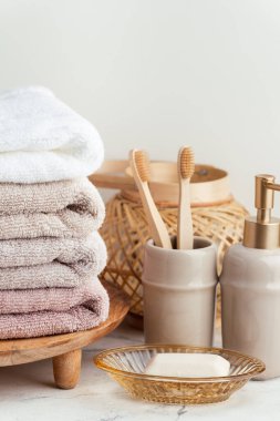Sabun ve diş fırçalarının yanında bir yığın temiz yumuşak havluyla klasik altın banyo malzemeleri. Beyaz arka planda banyo aksesuarları olan beyaz, pembe ve bej havlular..