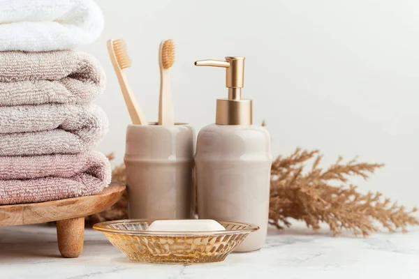 stock image Vintage golden bath supplies with stack of clean soft towels next to soap and toothbrushes. White, pink and beige towels with bathroom accessories on the white background.