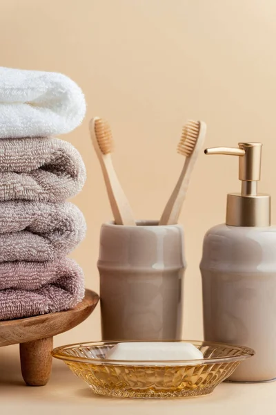 stock image Vintage golden bath supplies with stack of clean soft towels next to soap and toothbrushes. White, pink and beige towels with bathroom accessories on the beige background.