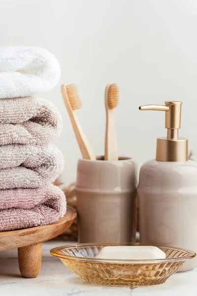 stock image Vintage golden bath supplies with stack of clean soft towels next to soap and toothbrushes. White, pink and beige towels with bathroom accessories on the white background.