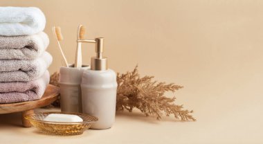 Sabun ve diş fırçalarının yanında bir yığın temiz yumuşak havluyla klasik altın banyo malzemeleri. Beyaz, pembe ve bej havlular. Bej arka planda banyo aksesuarları var..
