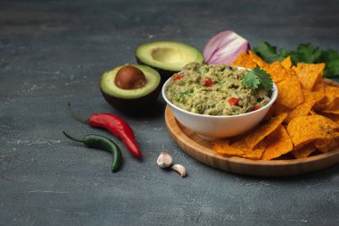 Beyaz kase, gri beton arka planda nachos ile geleneksel Meksika guacamolesi. Avokado, kişniş, soğan, acı biber ve limon karışımı soslu tortilla cipsi.