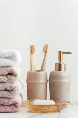 Sabun ve diş fırçalarının yanında bir yığın temiz yumuşak havluyla klasik altın banyo malzemeleri. Beyaz arka planda banyo aksesuarları olan beyaz, pembe ve bej havlular..