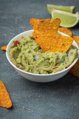 Beyaz kase, gri beton arka planda nachos ile geleneksel Meksika guacamolesi. Avokado, kişniş, soğan, acı biber ve limon karışımı soslu tortilla cipsi.
