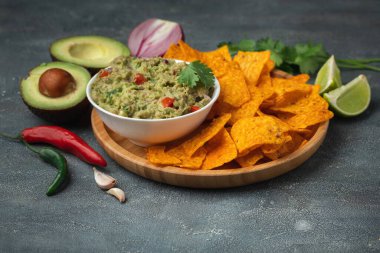 Beyaz kase, gri beton arka planda nachos ile geleneksel Meksika guacamolesi. Avokado, kişniş, soğan, acı biber ve limon karışımı soslu tortilla cipsi.