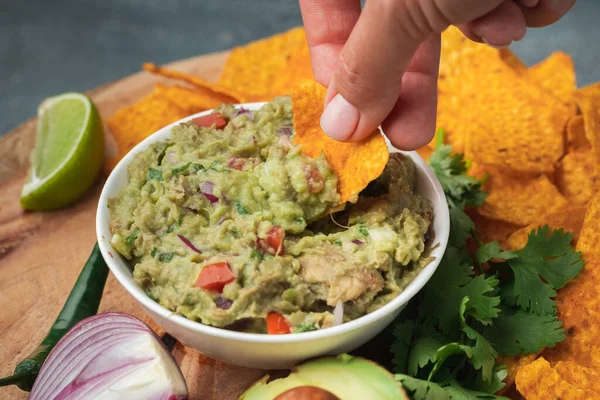 Kadın nachos 'u ahşap arka planda lezzetli guacamole sosuna daldırıyor. Avokado, kişniş, soğan, acı biber ve limonun yanında tortilla cipsi. Geleneksel Meksika yemekleri