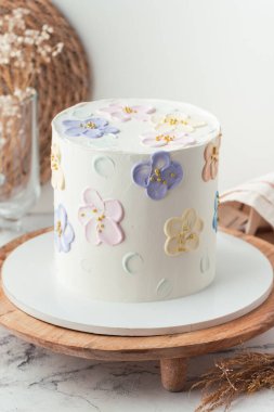 Pastel tereyağlı çiçeklerle süslenmiş beyaz krem peynirli doğum günü pastası. Ahşap pasta standındaki bir kız için şık bir pasta..