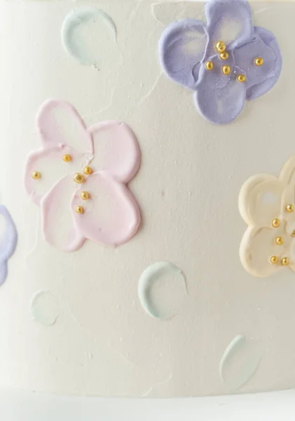 Close up of birthday cake with white cream cheese frosting decorated with pastel butter cream flowers. Stylish smears on cake textured background.