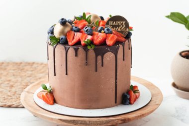 Erimiş siyah çikolata damlalarıyla süslenmiş sütlü çikolatalı doğum günü pastası ve taze yaz meyveleri: üstünde çilek ve yabanmersini. Beyaz arkaplan