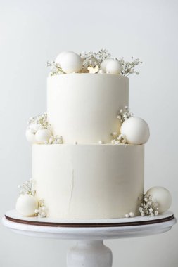 Beyaz çikolata kaplı büyük ranza düğün pastası ve beyaz arka planda beyaz çikolata küreleri ile süslenmiş..