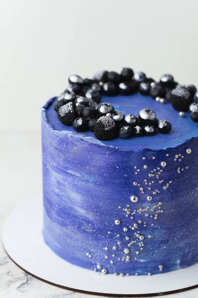 Birthday cake with blue cream cheese frosting decorated with blueberries covered with silver kandurin. Cosmic cake or space themed cake on the white background.